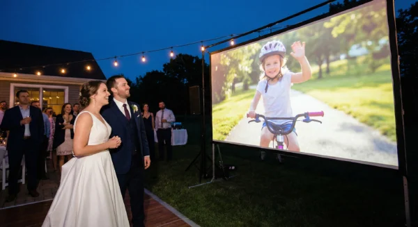 Bride and groom watch the bride's childhood life journey video on a large screen at their wedding reception.
